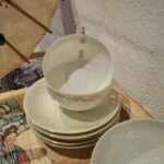 En stabel af hvide vintage tekopper med guldkanter og undertallerkener, som en del af et tesæt, på et mønstret træfad.