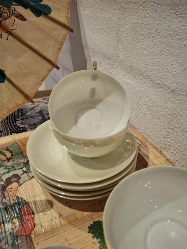 En stabel af hvide vintage tekopper med guldkanter og undertallerkener, som en del af et tesæt, på et mønstret træfad.
