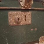 Et nærbillede af en rusten lås på en mørkegrøn vintage rejsekuffert.