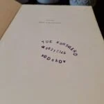 Inderside af bogen 'Wolf med Paraplyen' med et lilla stempel, der viser 'Tue Korsgård 98253148 Vodskov'.