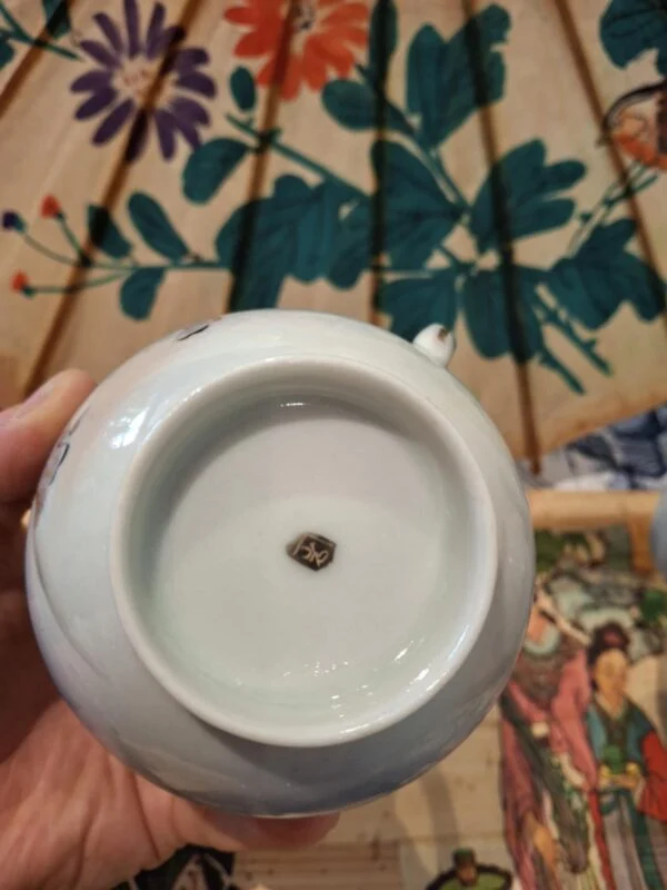 En lys underside med fodring og et lille mørkt mærke, holdt foran en papirparaply med blomstermotiv.