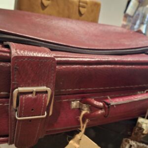 En dybrød vintage læderkuffert med spænder og lynlås, der viser strukturerede detaljer og spænde. 'Echtes Leder' mærke.