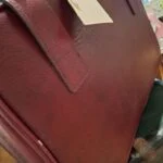 Et nærbillede af et af de kromfarvede spænder på den røde vintage læderkuffert, der viser patina og sølvfarvede metaldele.