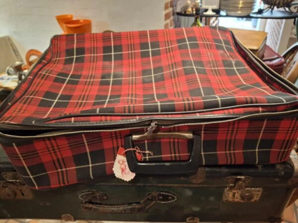 En rødrutet vintage kuffert med sort og beige, placeret oven på en mørkegrøn kuffert, med et lille hjertevedhæng.