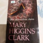 Forsiden af bogen 'Den allersidste dans' af Mary Higgins Clark, med en illustration af en sko på brosten.