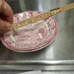 Hånd måler en engelsk fajance skål med rund kant, 15,5 cm, rød transferprint af herregårdslandskab.