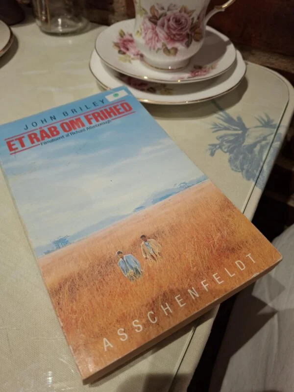 Forsiden af bogen 'Et råb om frihed' af John Briley, der viser to mænd i et gyldent græslandskab under en blå himmel.