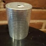 Cylinderformet metalsparebøsse med vandrette riller, mærket top og synlige overfladespor.