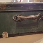 En mørkegrøn vintage Vulkolit rejsekuffert lukket, med synlige rustne beslag og håndtag. 'Vulkolit' logo synligt.