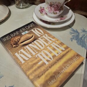 Forsiden af bogen 'To Kvinder – To Liv' af Iris Rainer Dart, med muslingeskaller og en illustrativ baggrund.