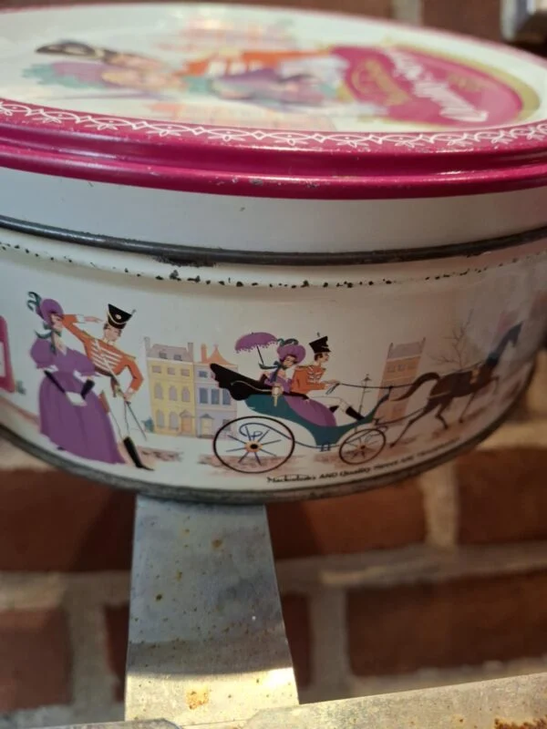 En lille rund vintage Quality Street dåse med rødt låg og detaljerede illustrationer, set fra siden.