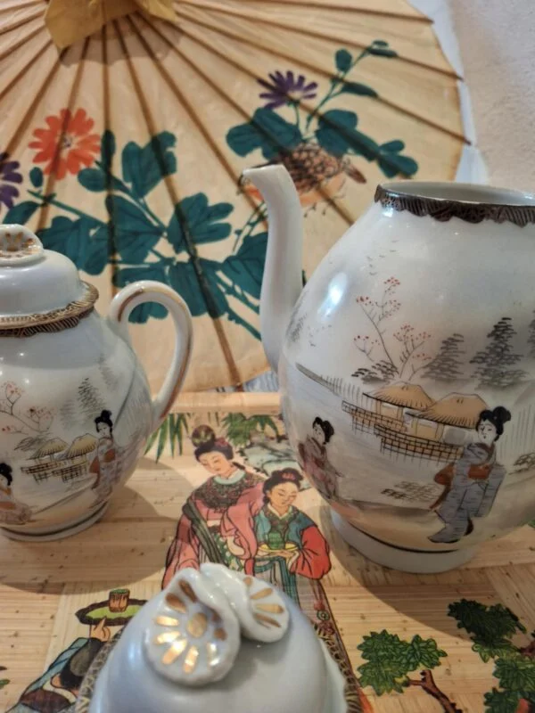 To kander med japanske figurmotiver og gyldne kanter; et låg ligger foran den høje kande.