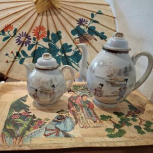 To vintage japanske porcelænstekander med damemotiver på en bambusbakke, under en japansk papirparaply.