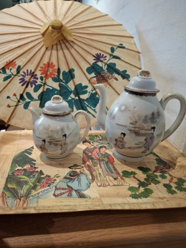 To vintage japanske porcelænstekander med damemotiver på en bambusbakke, under en japansk papirparaply.