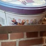 En lille rund vintage Quality Street dåse med rød kant og illustrationer af et julepar der skøjter.