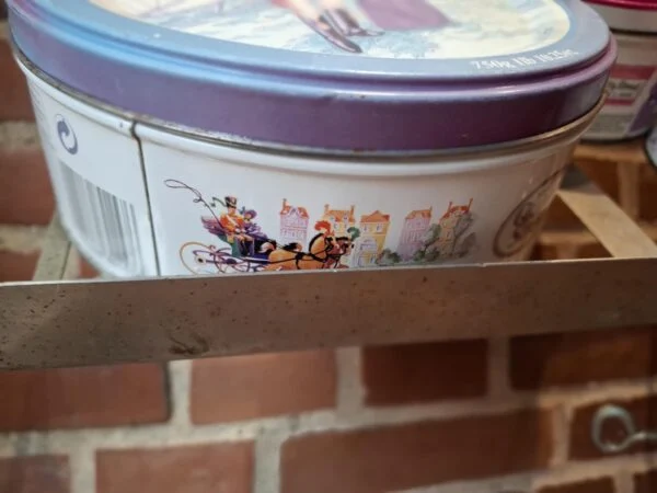 En lille rund vintage Quality Street dåse med rød kant og illustrationer af et julepar der skøjter.