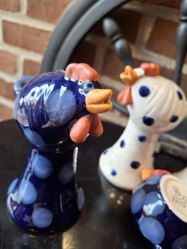 To keramik hønefigurer, den ene blå med prikker og den anden hvid med prikker, med et smilende udtryk og orange næb og kam.