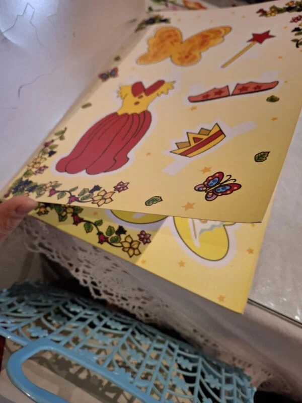Opslået 'Min egen fe' påklædningsbog, viser udklipsark med kjoler, kroner, tryllestav og sommerfugle.