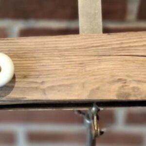 En rustik knagerække fremstillet af lyst drivtømmer, monteret med tre hvide porcelænsknopper med messingdetaljer.