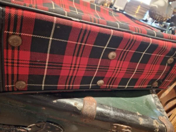 Et kig på undersiden af den rødrutede vintage kuffert, der viser de støttende nitter og slid på materialet.