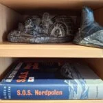 En mørk patineret keramikfigur af en søløve med et detaljeret udtryk på en træhylde.