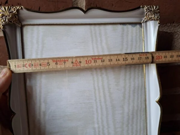 Nærbillede af et øvre højre hjørne af en hvid vintage fotoramme med guldkant og detaljeret ornamentik.