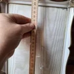 En elegant hvid vintage fotoramme med gyldne, ornamenterede detaljer i hjørnerne, stående oprejst med murstensvæg i baggrund.