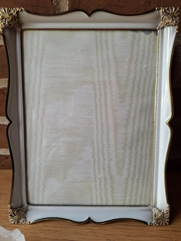 En stor, hvid fotoramme med guldkant og dekorative hjørner, stående bag to Holmegaard glasskåle (én frostet, én klar).
