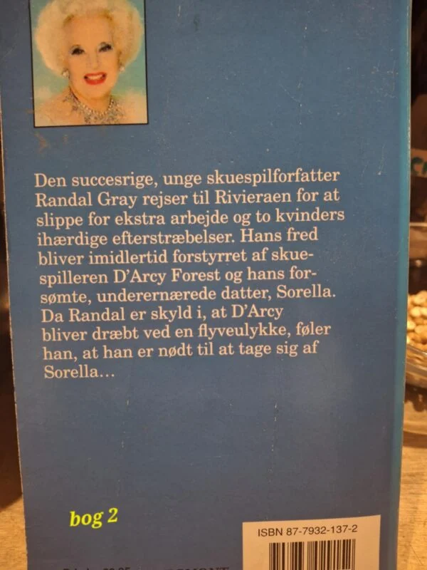En stak på fem bøger i forskellige farver og størrelser med en blomsterdekoreret kaffekop og småkager på en lyserød hækledug.