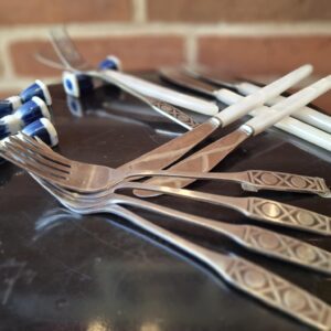 Et arrangement af vintage knive med perlemorsgreb og gafler med mønstrede stålhåndtag, sammen med blå-hvide porcelænsholdere.