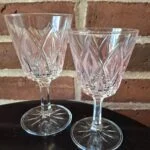 To klare glas på fod med svagt rosa felter i mønstret omkring kummen.