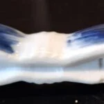 Nærfoto af en blå-hvid holder med buet midte og uskarp mærkning på den hvide underside.