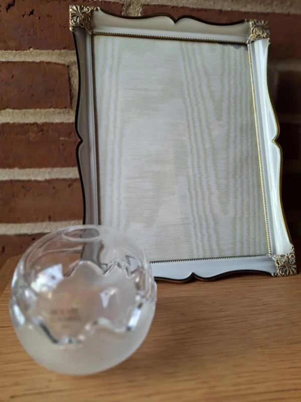En stor, hvid fotoramme med guldkant og dekorative hjørner, stående bag to Holmegaard glasskåle (én frostet, én klar).