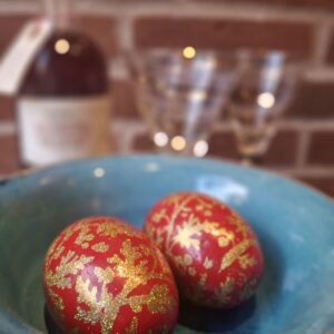 To skinnende røde trææg med guldglimmer, placeret i en blå keramikskål, med en flaske og cocktailglas i den slørede baggrund.