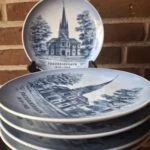 Flere Royal Copenhagen-platter med Frederikshavn Kirke er stablet foran en opretstående platte; varen sælges enkeltvis.