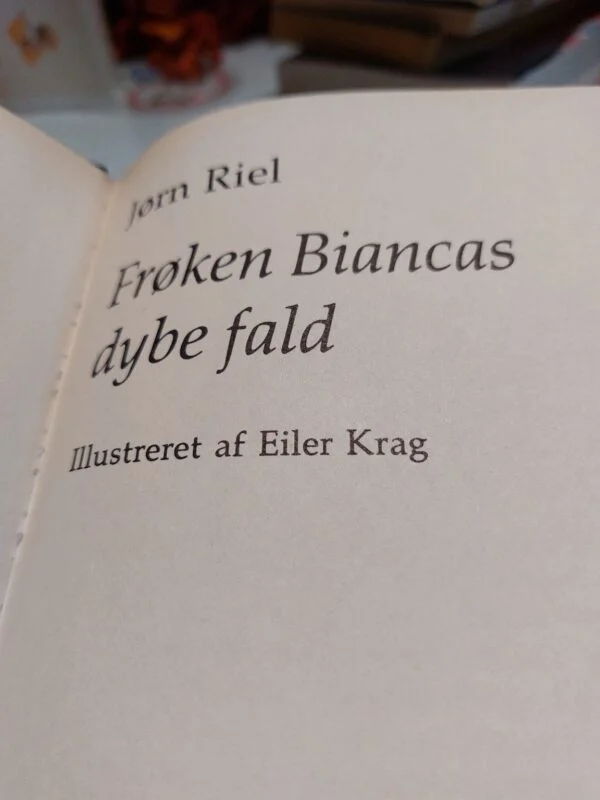 Nærbillede af bogryggen på 'Frøken Biancas dybe fald' af Jørn Riel, med grønt og beige design og gulddetaljer.