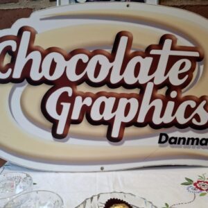 Et vintage krystalglas med facetmønster i forgrunden, et andet krystalglas og en krystalskål med chokolade i baggrunden, på en broderet hvid dug.