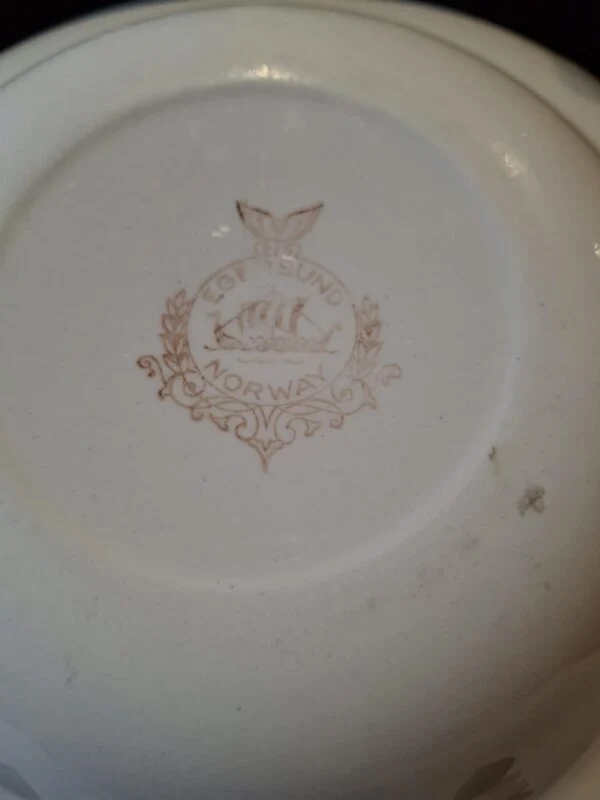 Undersiden af en tallerken med et brunligt Egersund Norway-stempel med skib og fugl.