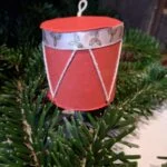Et lille, håndlavet juletromme ophæng i rød og grøn med julemotiver af kristtjørn. Hænger i juletræets grangrene.