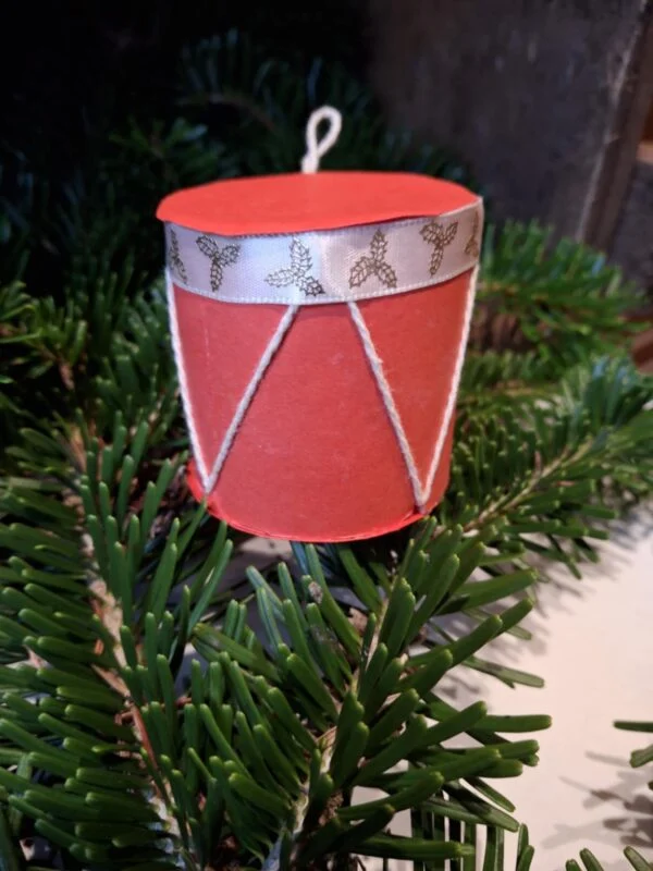 Et lille, håndlavet juletromme ophæng i rød og grøn med julemotiver af kristtjørn. Hænger i juletræets grangrene.
