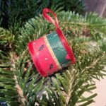 Et håndlavet juletromme ophæng i sølv med et diskret mønster af hjerter og stjerner, sat på juletræets grangrene.