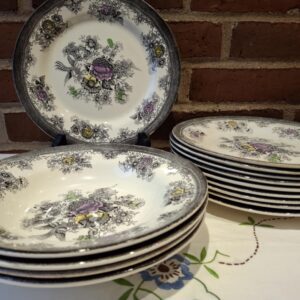 En stak dybe Egersund tallerkener i beige fajance, dekoreret med håndmalede sorte streger af fugle og blomster, suppleret med lilla og gule detaljer.