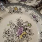 Dyb tallerken med fugle og farvede blomster set skråt ovenfra; flere beslægtede tallerkener står bagved.