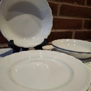 En stak hvide, flade Hanley Ware 'Satin White' tallerkener med elegant reliefkant, placeret på hvid dug foran en murstensvæg.