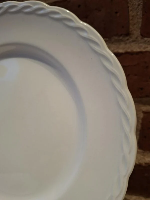 Nærbillede af kanten på en hvid Hanley Ware 'Satin White' flad tallerken, der fremhæver den flettede reliefdetalje.