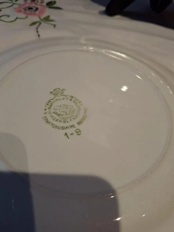 Bagsiden af en hvid Hanley Ware 'Satin White' flad tallerken med grønt stempeltekst 'HANLEY WARE SHAZENGLAND BROOLEY & CO STAFFORDSHIRE IRONSTONE'.