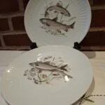 To hvide Schumann Arzberg-tallerkener med fiskemotiver og en netlignende reliefkant