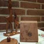 Vintage Lütjhøe Wood sennepskrukke i teaktræ med glasindsats og tilhørende ske. Billedet viser undersiden af træfadet med mærke. Teaktræsrådyr i baggrunden.