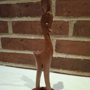 En elegant vintage rådyrfigur af mørkt teaktræ, stående oprejst på en hvid overflade foran en murstensvæg.