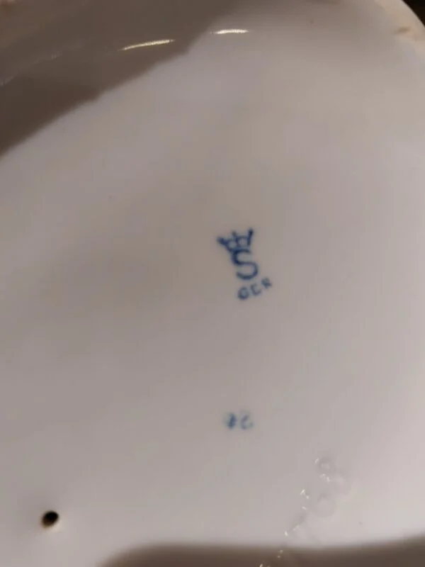 Billede af bunden af en porcelænsfigur, der viser mærket en krone med et 'S' og teksten 'GOR' nedenunder i blåt.